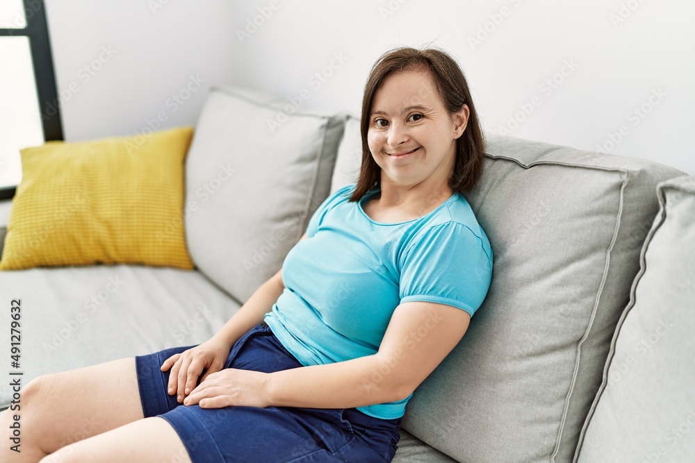 Brunette woman with down syndrome sitting on the sofa at the living room Brunette woman with down syndrome sitting on the sofa at the living room
