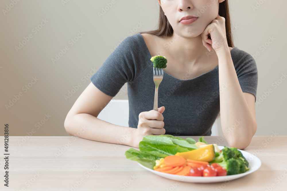unhappy asian women is on dieting time looking at broccoli on the fork. girl do not want to eat vegetables and dislike taste unhappy asian women is on dieting time looking at broccoli on the fork. girl do not want to eat vegetables and dislike taste