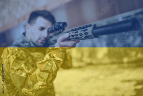 Strong military soldier targets and holds a large gun in the destoy building on ukraine flag background. photo