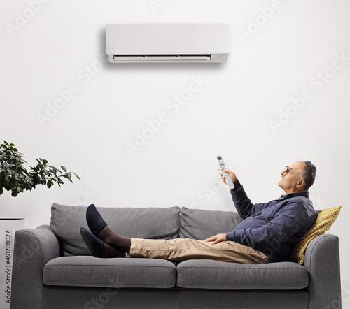 Fotografija Mature man on a sofa putting the air conditioning on