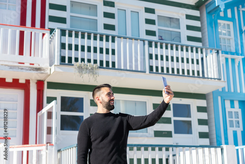 Tourist boy holding his cell phone in front of the houses in Costa Nova, Portugal.