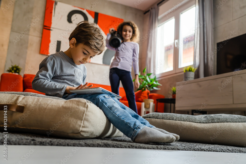 Children having fun at home alone two siblings brother and sister girl holding wifi speaker listening to the music while her brother is playing video games using digital tablet having fun at home
