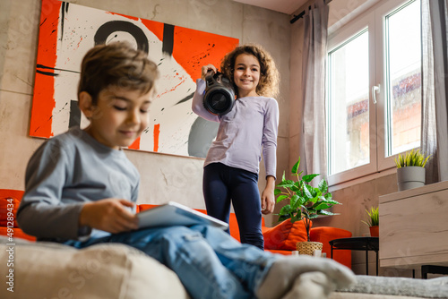 Children having fun at home alone two siblings brother and sister girl holding wifi speaker listening to the music while her brother is playing video games using digital tablet having fun at home © Miljan Živković