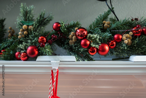 A decorated white Christmas mantle with pine garland and strung red ball ornaments photo