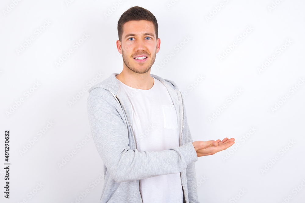 young caucasian man wearing casual clothes over white background says: wow how exciting it is, has amazed expression, shows something on blank space with palm. Advertisement concept.