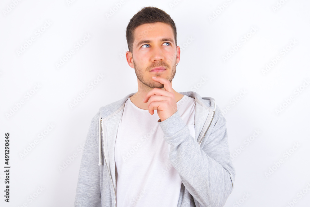 Shot of contemplative thoughtful young caucasian man wearing casual clothes over white background keeps hand under chin, looks thoughtfully upwards. Shot of contemplative thoughtful young caucasian man wearing casual clothes over white background keeps hand under chin, looks thoughtfully upwards.