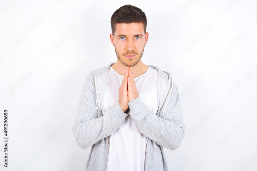 young caucasian man wearing casual clothes over white background keeps palms pressed together in front of her having regretful look, asking for forgiveness. Forgive me please. young caucasian man wearing casual clothes over white background keeps palms pressed together in front of her having regretful look, asking for forgiveness. Forgive me please.