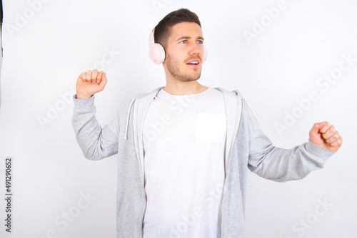 young caucasian man wearing casual clothes over white background, dancing and listening music with headphones.
