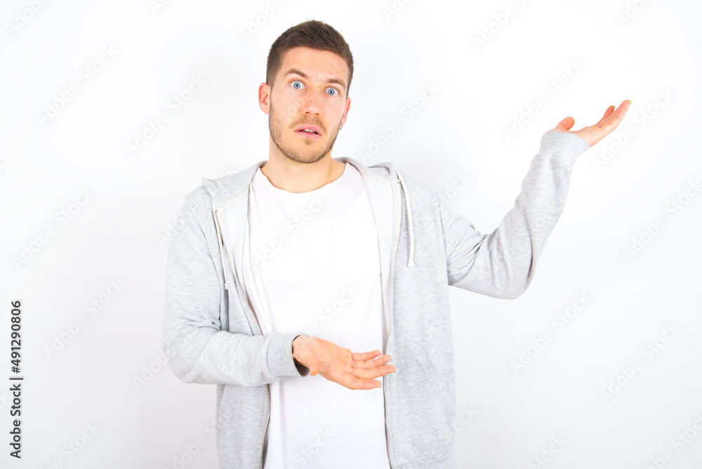 young caucasian man wearing casual clothes over white background pointing aside with both hands showing something strange and saying: I don't know what is this. Advertisement concept. young caucasian man wearing casual clothes over white background pointing aside with both hands showing something strange and saying: I don't know what is this. Advertisement concept.
