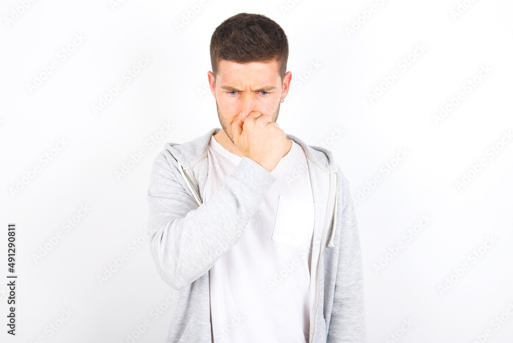 young caucasian man wearing casual clothes over white background , holding his nose because of a bad smell. young caucasian man wearing casual clothes over white background , holding his nose because of a bad smell.