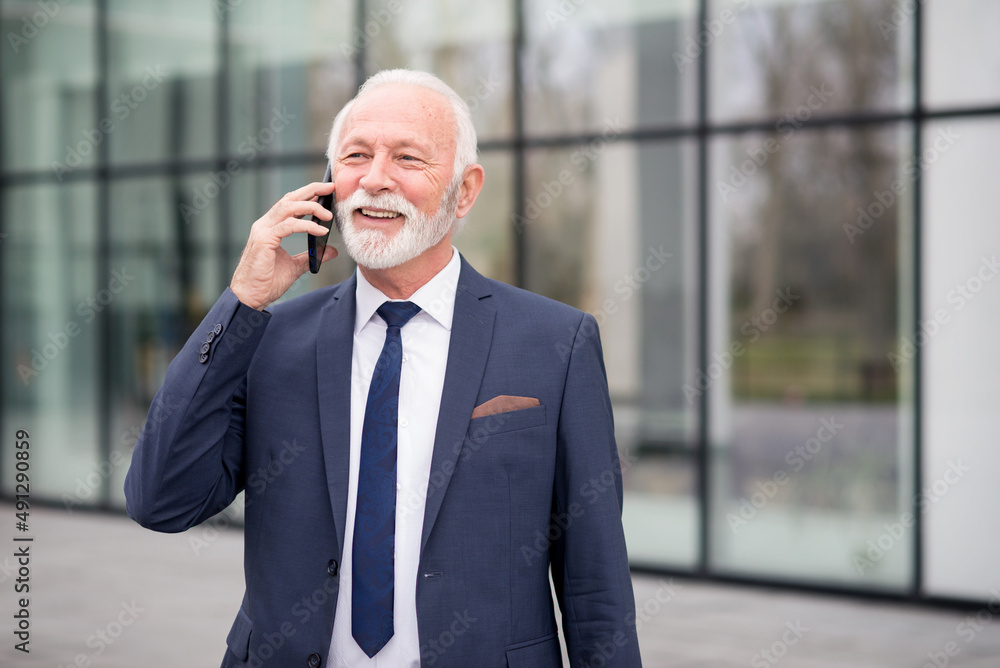 Senior smiling businessman using smart phone in front of the office building. Senior smiling businessman using smart phone in front of the office building.