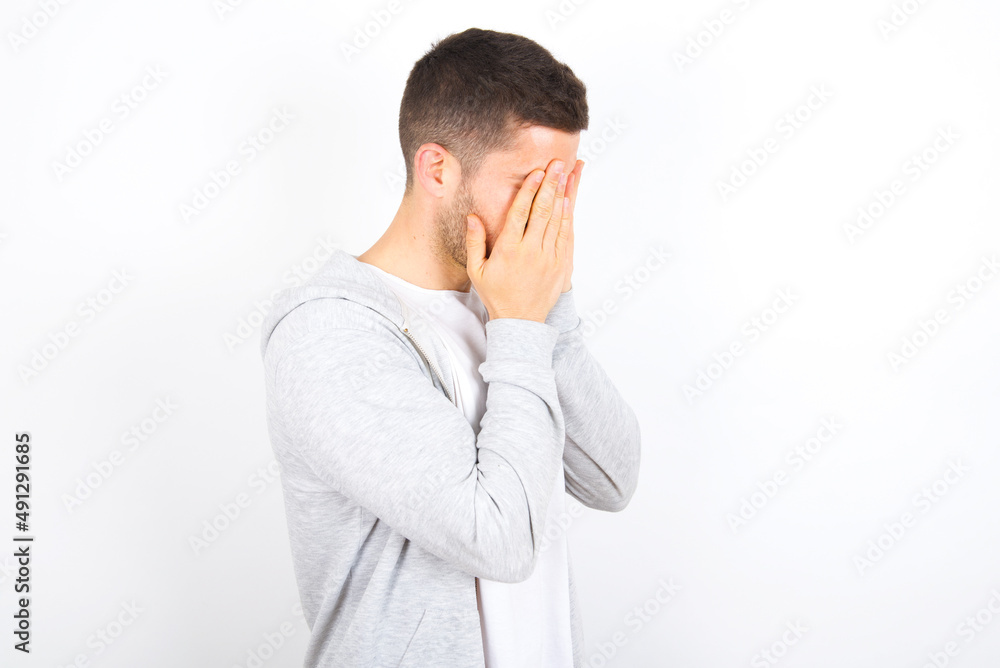 Sad young caucasian man wearing casual clothes over white background covering face with hands and crying. Sad young caucasian man wearing casual clothes over white background covering face with hands and crying.