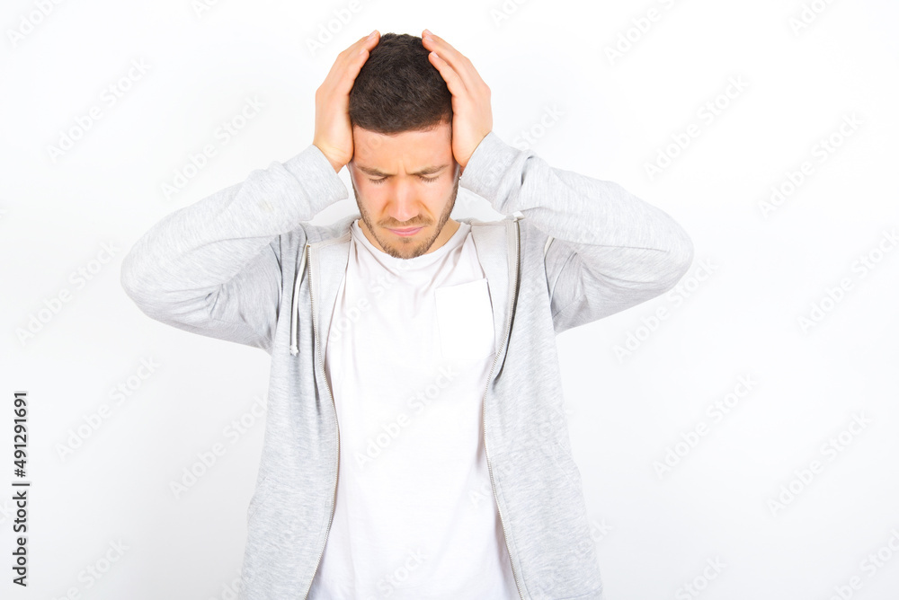 young caucasian man wearing casual clothes over white background  holding head with hands, suffering from severe headache, pressing fingers to temples