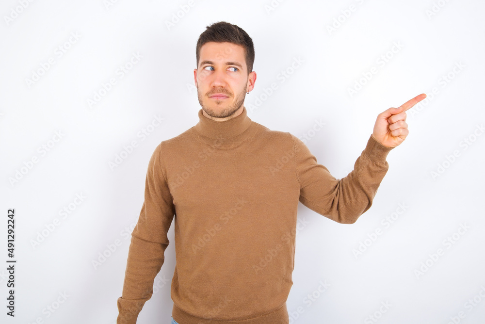 young caucasian man wearing knitted turtleneck over white background points at copy space and advertises something, advices best price. young caucasian man wearing knitted turtleneck over white background points at copy space and advertises something, advices best price.