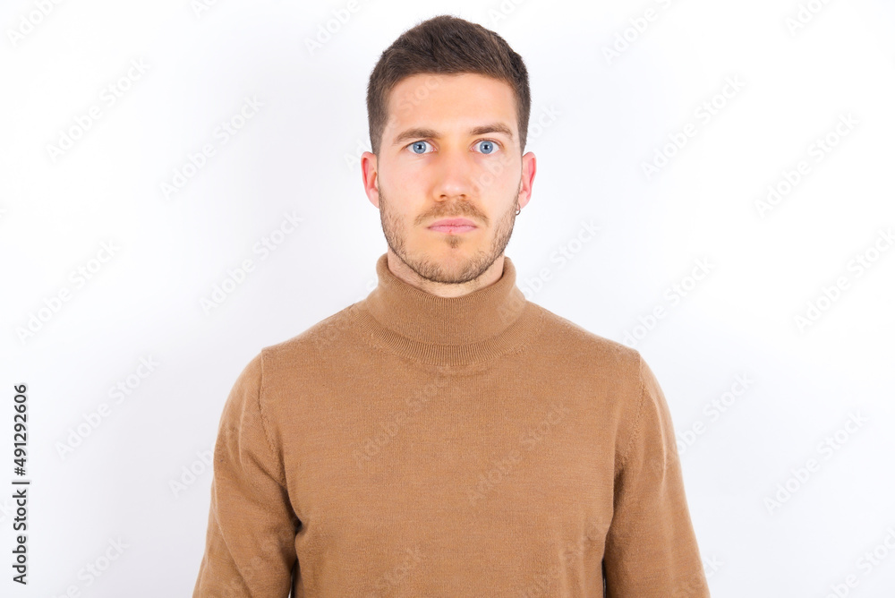 Obraz premium Displeased young caucasian man wearing knitted turtleneck over white background frowns face feels unhappy has some problems. Negative emotions and feelings concept