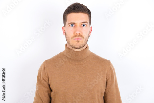 Displeased young caucasian man wearing knitted turtleneck over white background frowns face feels unhappy has some problems. Negative emotions and feelings concept