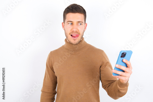 Photo of nice pretty young caucasian man wearing knitted turtleneck over white background demonstrate phone screen hold hair tails