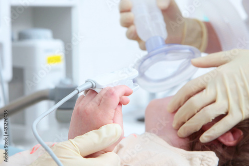 Child s hand with a device for measuring the level of oxygen in the blood in close-up. Coming out of anesthesia. A device for measuring oxygen concentration.Face is out of focus.