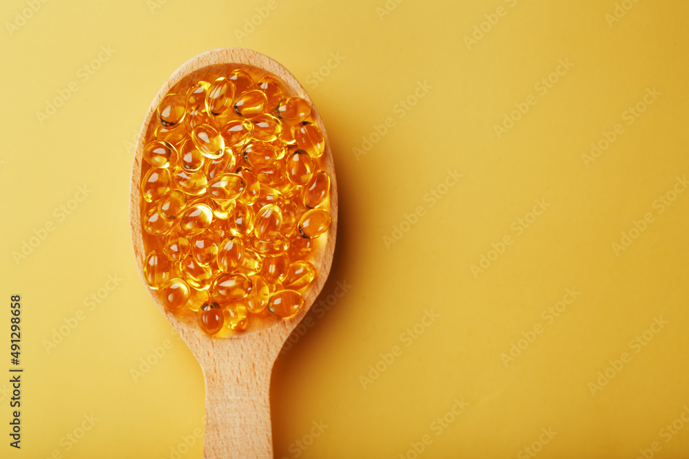 Fish oil capsules in a wooden spoon on a bright yellow background Fish oil capsules in a wooden spoon on a bright yellow background