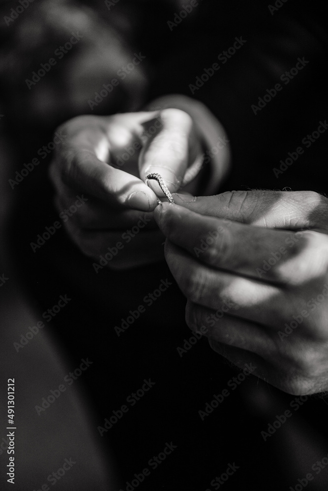 The groom on his wedding day holds the wedding ring in his hands in a hotel room Male hand and wedding ring Close up Black and White photo