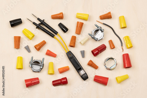 Horizontal flat layout of assorted color wire nuts, connectors, electricity tester, and wire on light wood textured background