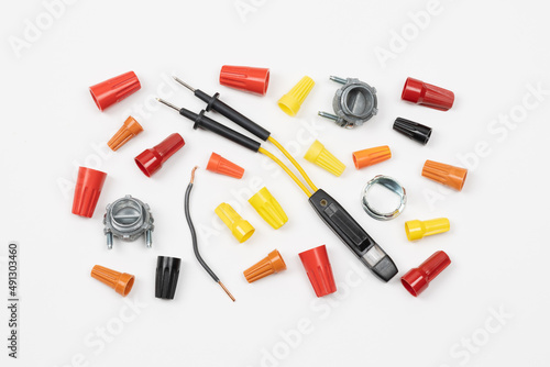 Horizontal flat layout of assorted color wire nuts, connectors, electricity tester, and wire on white background