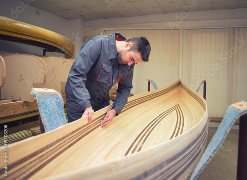Fényképezés Young carpenter making wooden canoe in his workshop.
