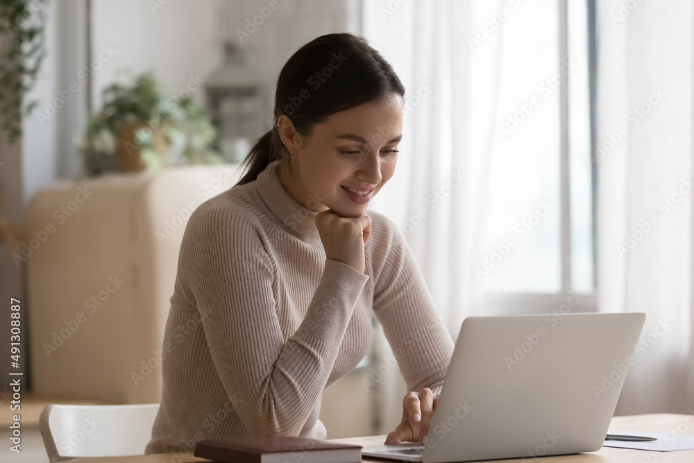 Young smiling woman sit at table in domestic kitchen with laptop, make order, choose products on-line, enjoy easy comfort electronic retail services, working from home use modern technology concept Young smiling woman sit at table in domestic kitchen with laptop, make order, choose products on-line, enjoy easy comfort electronic retail services, working from home use modern technology concept