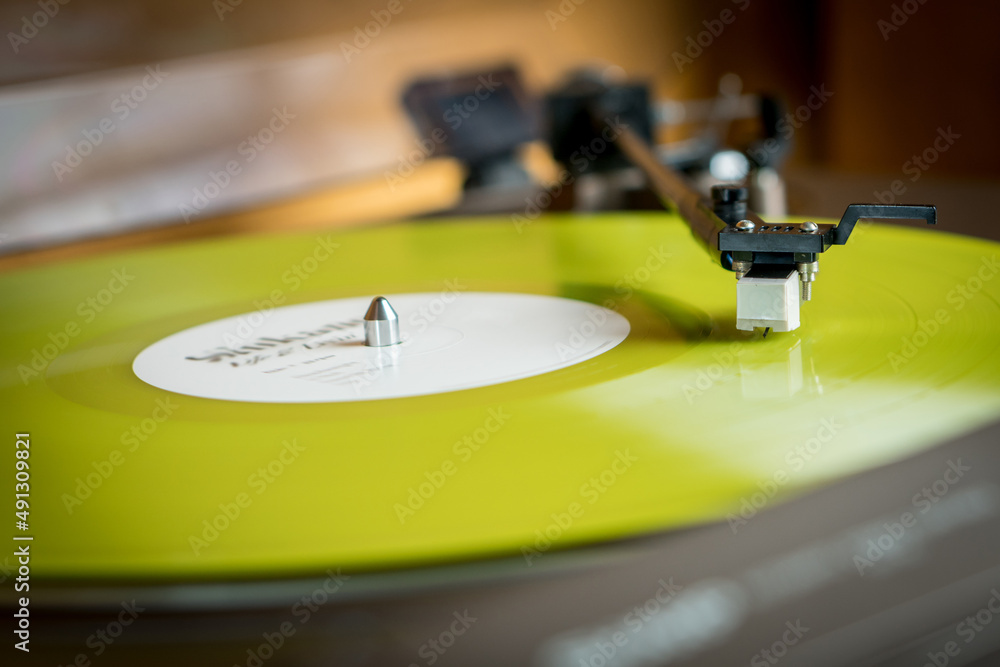 Obraz premium Closeup view of a tonearm and turntable playing color yellow vinyl record.