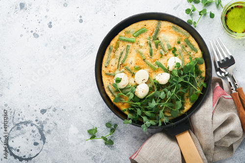 Omelet with spinach, green beans, potato and spinach healthy food in black frying pan on grey stone old rustic background. Traditional frittata for breakfast Eggs tortilla Top view flat lay Copy space