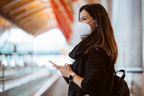 Tourist woman at the airport waiting for her flight. Wearing a mask for covid 19 protection using her smartphone while waiting. Lifestyle. Travel