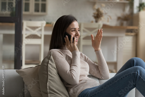 Happy beautiful young woman relax on sofa holds smartphone taking to friend, share news enjoy pleasant personal conversation. Mobile network operator usage, phone call activity, communication concept