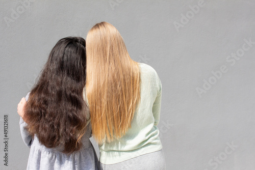 Tableau sur toile two girls with different color of hair are standing and hugging each other, grey