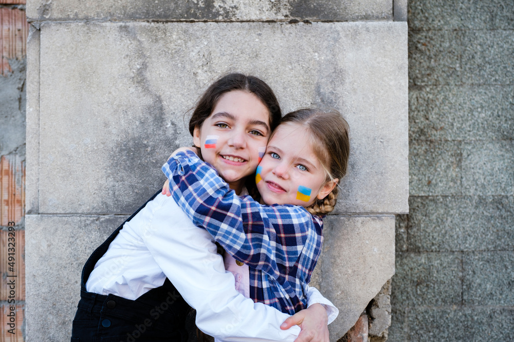 Portrait of two little girls embracing with Russian and Ukrainian flags on the faces. Concept of peace, stop the war and friendship of children against hate people