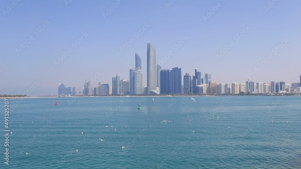 Abu Dhabi cityscape during sunny day with seagulls flying around, view from seaside Abu Dhabi cityscape during sunny day with seagulls flying around, view from seaside