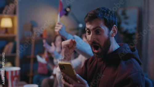Concentrated bearded man looking attentively at his device screen and rejoicing while looking at results of sports betting during football game. Male fans cheering at home concept. photo
