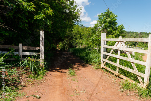 Entrada de sítio com muita vegetação em volta, porteira rústica e lindo céu azul na região de Igarapé, Minas Gerais.