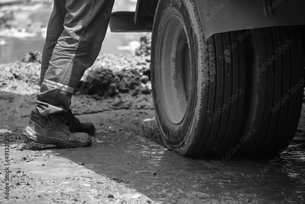 person standing on muddy asphalt next to a wheel of a vehicle person standing on muddy asphalt next to a wheel of a vehicle