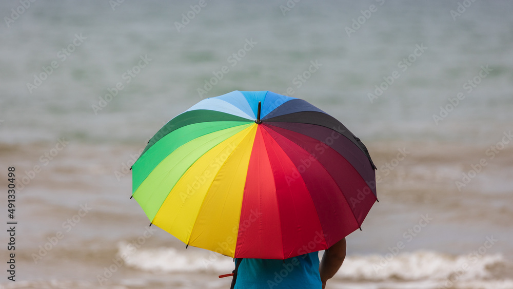 Man hold a rainbow color umbrella during sunny day at beach