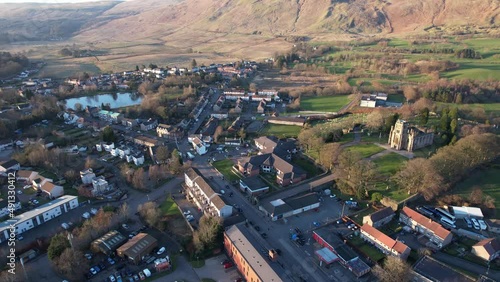 Low level aerial footage of a Scottish village and glen surrounded by hills. A bright sunny day with a low sun casting long shadows and a restored church clock tower. photo