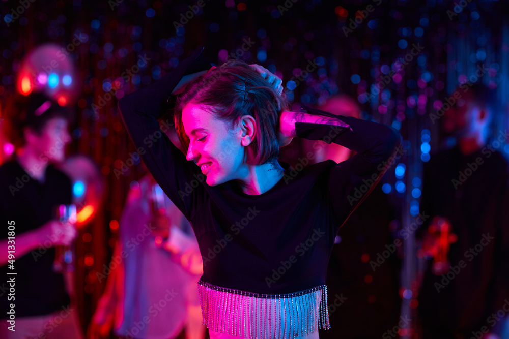 Waist up portrait of carefree young woman dancing at party in neon lights, copy space