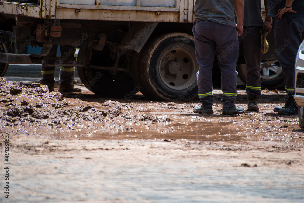 construction workers standing on muddy asphalt next to a vehicle construction workers standing on muddy asphalt next to a vehicle
