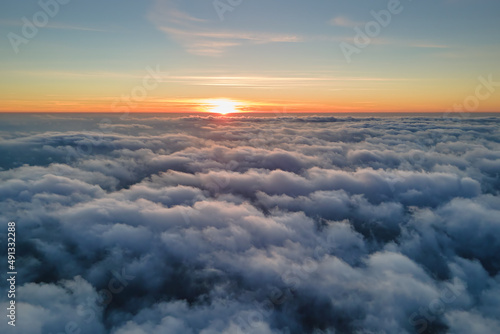 Aerial view from above at high altitude of dense puffy cumulus clouds flying in evening. Amazing sunset from airplane window point of view