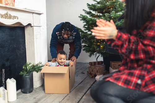 Playful mixed-race toddler pretends to be a Christmas Present by hiding in a carton box. High quality photo