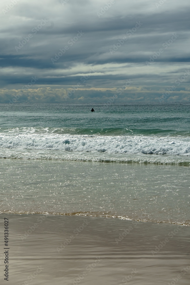 View of sand, surf, sea and overcast cloudy sky, with a single person swimming. Currumbin Beach, Queensland, Australia View of sand, surf, sea and overcast cloudy sky, with a single person swimming. Currumbin Beach, Queensland, Australia