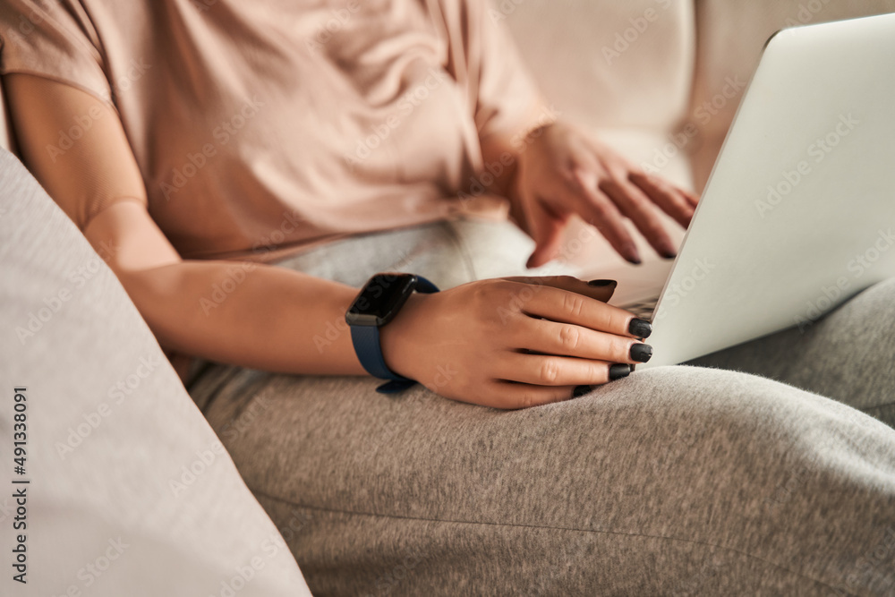 Naklejka premium Woman with prosthesis limb sitting at the sofa and using laptop while woking or relaxing at home