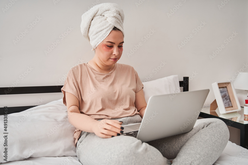 Woman with bionic limb is sitting on bed and looking at the screen of the laptop Woman with bionic limb is sitting on bed and looking at the screen of the laptop
