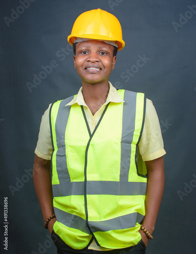African Nigerian female construction or civil engineer, architect or builder with yellow safety helmet and green reflective jacket