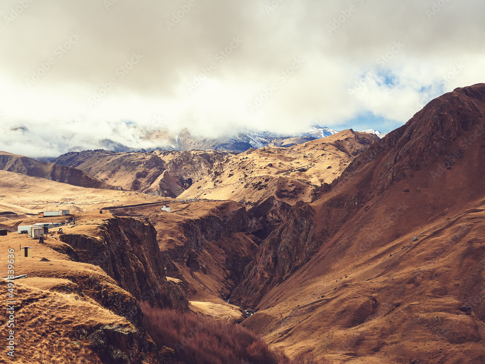 Fototapeta premium A mighty snowy Elbrus hides behind the clouds in the distance. Jily su mountain valley in autumn