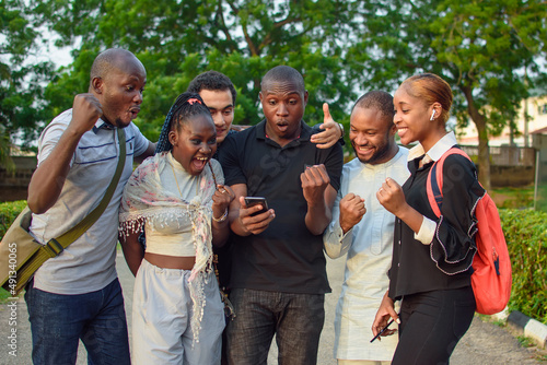 Groups of african friends, students or sport lovers consisting of male and female individuals, happily staring into the smart phone with various jubilation gestures and expressions